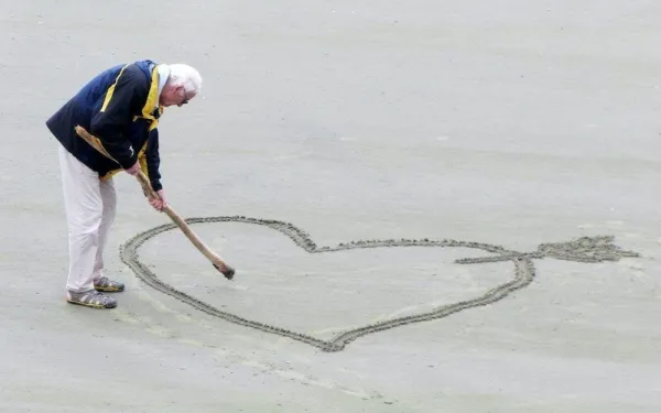 Starší muž kreslí srdce do písku